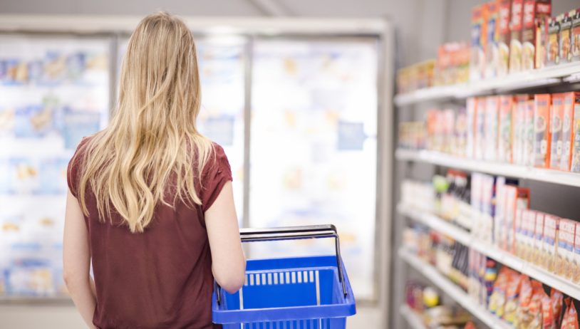 woman holding a basket looking at frozen food fridge