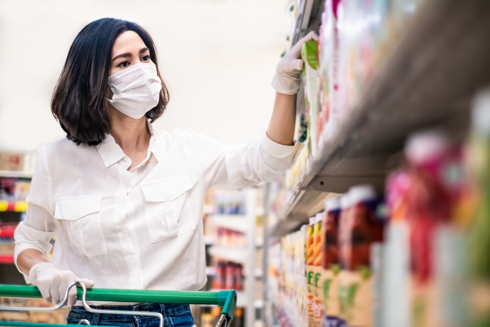 Asian woman wearing face mask and rubber glove push shopping cart in suppermarket departmentstore.