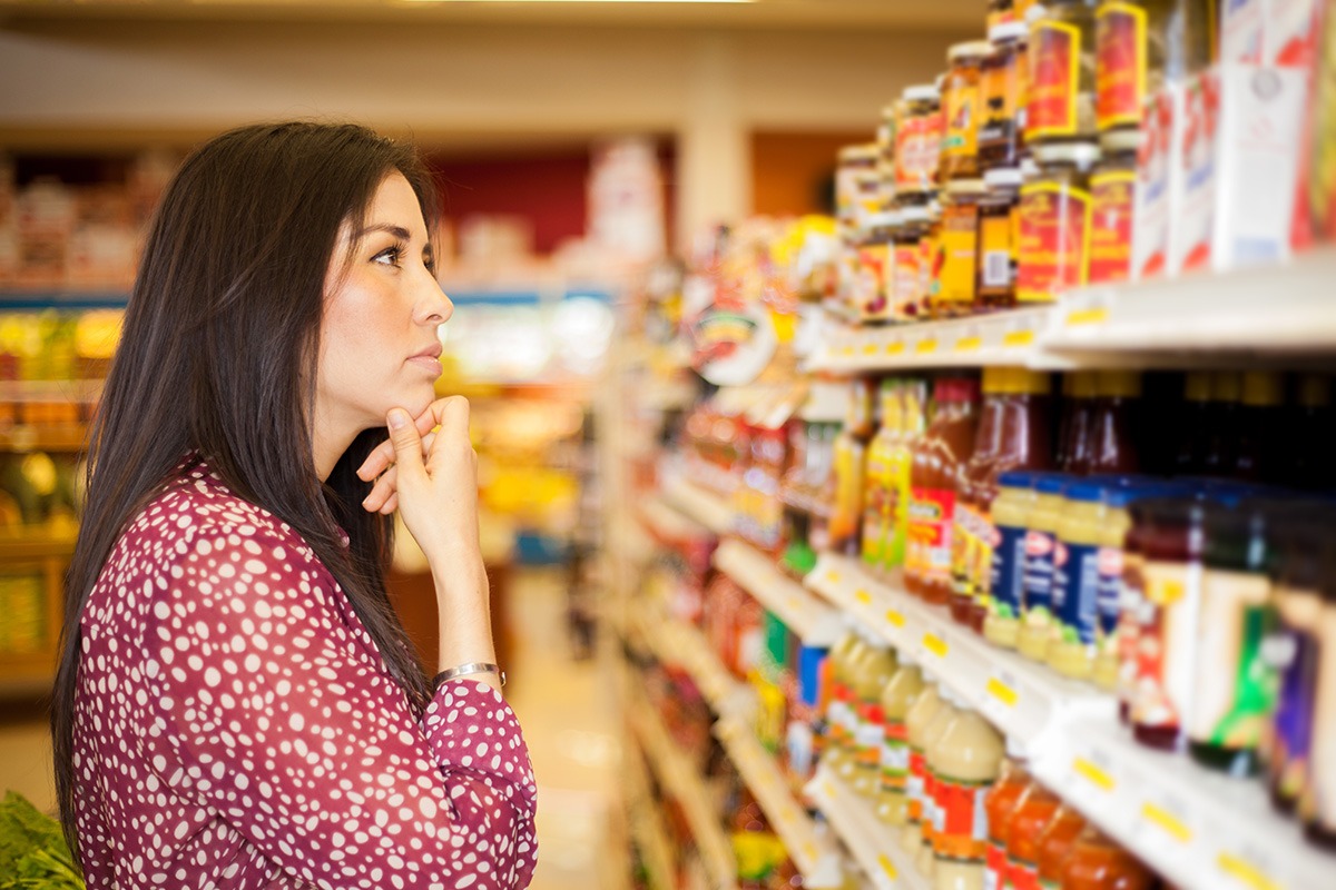 A woman looking at some shelves in a supermarket trying to decide what to buy