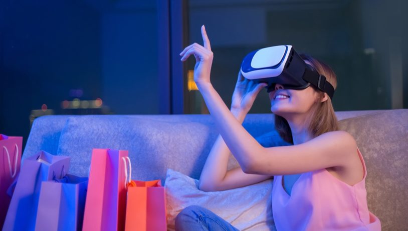 woman shopping online with VR headset on sofa colorful shopping bags around