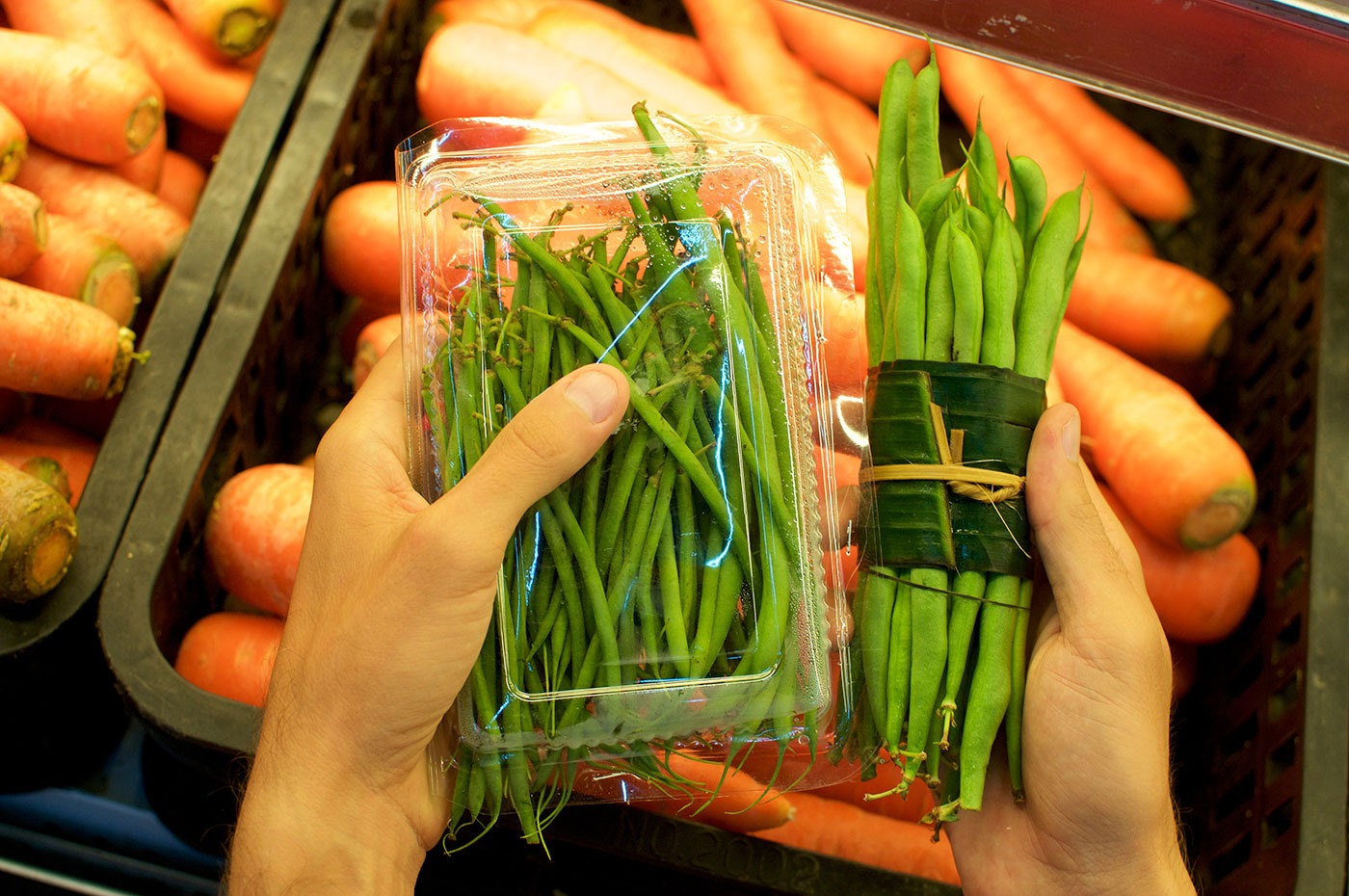 Beans bundled in a plastic package and other beans wrapped in Banana leaf held in female hands